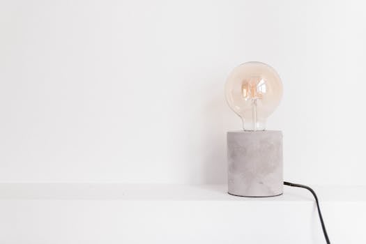 Close-up of an incandescent light bulb on a modern concrete base against a white background.