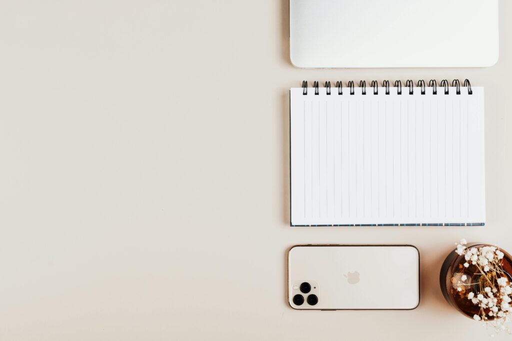 Flat lay of a modern workspace featuring a notebook, smartphone, and a decorative plant in a serene minimalist setting.